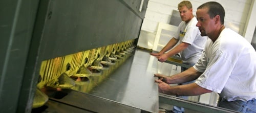 Two men pulling out a metal slab out a large machine.